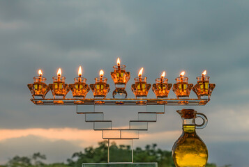 Obraz premium Crystal festive menorah and burning candles with olive oil as symbol of Hanukkah - Jewish Holiday of Miracle Light. Blurred background of evening overcast sky