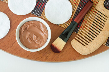 Red moroccan bentonite clay in a small white bowl, make-up brush and hairbrush. Clay texture close up. Diy facial or hair mask, body wrap recipe. Natural beauty treatment and spa. Top view, copy space