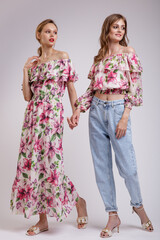 Two high fashion models in long dress with a red floral pattern, blouse, blue jeans. Beautiful young women. Studio shot, portrait. White background.  Slim figure. Make up, hairstyle