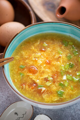 Close-up of chinese tomato egg-drop soup served in a turquoise bowl, vertical shot, selective focus