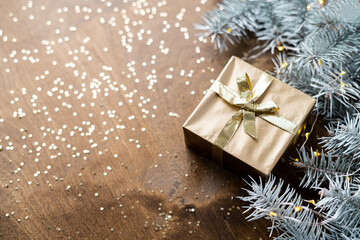 a golden gift box on a wooden table among fir branches with warm light bulbs