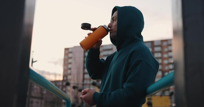Man on the workout sports ground drinks a tea from thermos