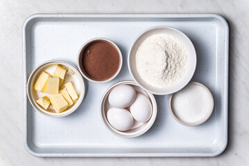 Baking ingredients in bowls: flour, eggs, sugar, butter. White background.