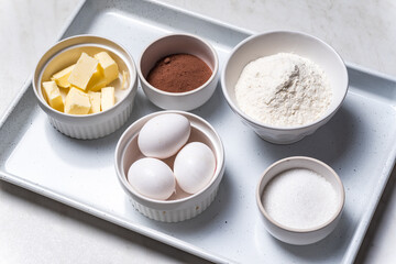 Baking ingredients in bowls: flour, eggs, sugar, butter. White background.