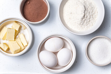 Baking ingredients in bowls: flour, eggs, sugar, butter. White background.