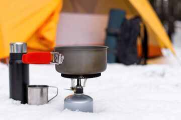 Fototapeta na wymiar Gas tourist burner and pot, against the background of the tent. Equipment for winter hiking, tourist cuisine.