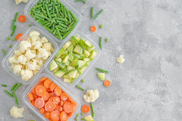 A variety of frozen vegetables in plastic containers on a gray concrete background. Healthy food....