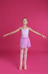 Little ballerina practicing dance moves on pink background