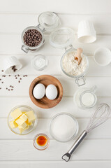 Ingredients for making muffins with chocolate chips. Eggs, butter, sugar, flour, vanilla, chocolate chips on a white wooden background. Recipe step by step. Top view.