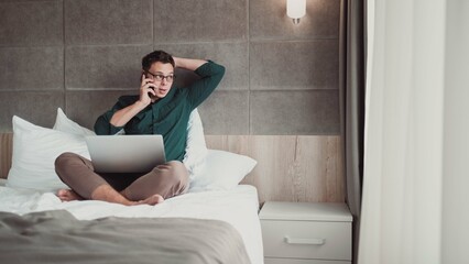 Man working at home on laptop and talking on the phone,  looking out the window