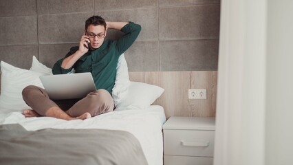 Young man working at home on laptop and talking on the phone