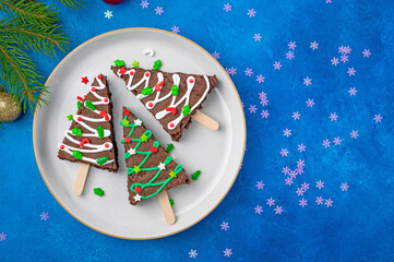 Christmas chocolate brownies with sugar glaze and sprinkles on a blue concrete background....