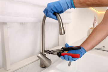 Man repairing water tap with wrench in kitchen, closeup