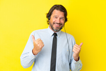 Telemarketer dutch man working with a headset isolated on yellow background with thumbs up gesture and smiling