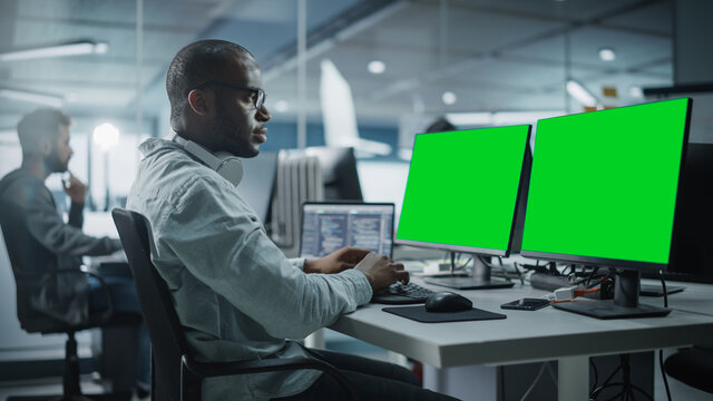 Multi-Ethnic Office: Black IT Programmer Working on Computer with Green Screen Chroma Key Display. Male Software Engineer Developing App, Program, Video Game. Terminal with Code Language.