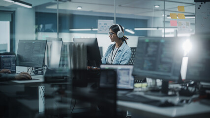 Diverse Office: Indian IT Programmer Working on Computer. Female Specialist Creating Innovative Software. Engineer Developing App, Program, Video Game. Wearing Headphones Listening Podcast, Music