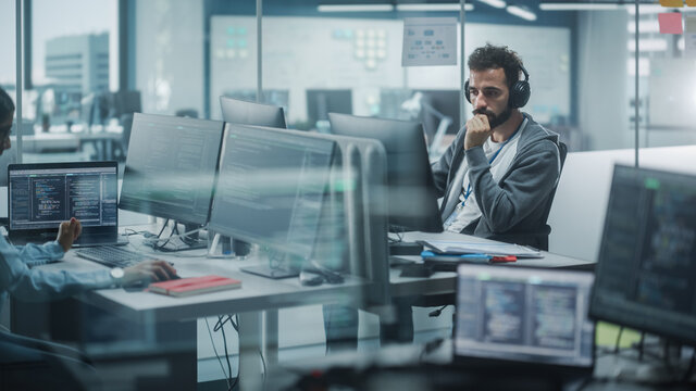 Diverse Office: White IT Programmer Working on Computer. Male Specialist Creating Innovative Software. Engineer Developing App, Program, Video Game. Wearing Headphones Listening Podcast, Music