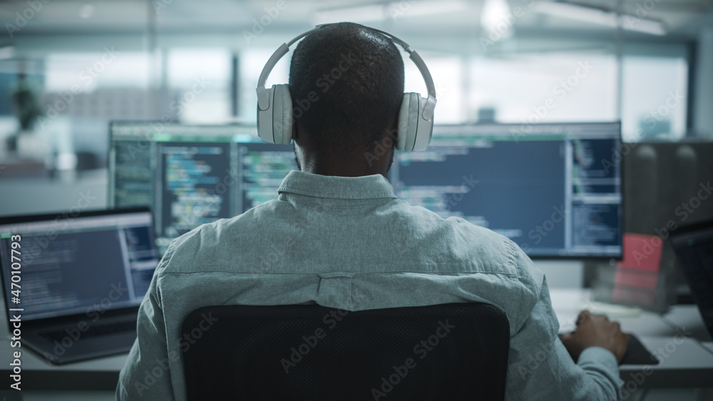 Aufkleber Office: Professional Black IT Programmer Uses Headphones while Working on Desktop Computer. Male Website Developer, Software Engineer Developing App, Video Game. Listening to Podcast, Music. Back View
