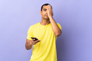 African American man over isolated purple background using mobile phone covering a eye by hand