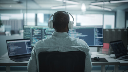 Office: Professional Black IT Programmer Uses Headphones while Working on Desktop Computer. Male...