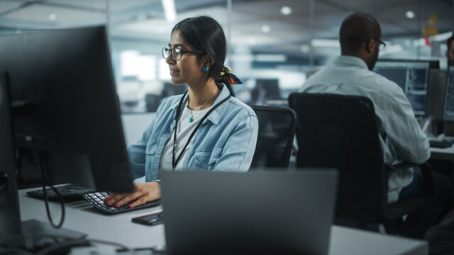 Diverse Office: Portrait of Talented Indian Girl IT Programmer Working on Desktop Computer in Friendly Multi-Ethnic Environment. Female Software Engineer Wearing Glasses Develop Inspirational App