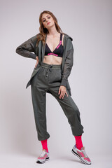 High fashion photo of a beautiful elegant young woman in a pretty green tracksuit, jacket, pants, sports bra, sneakers, pink socks posing over white background. Slim figure. Studio shot.