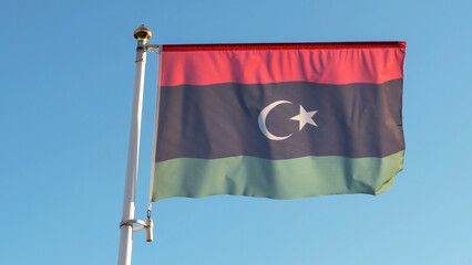 National flag of Islamic republic of Libya on a flagpole in front of blue sky with sun rays. Diplomacy concept.