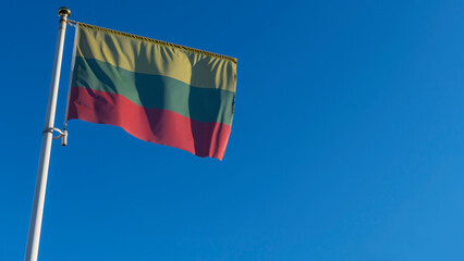 National flag of Lithuania on a flagpole in front of blue sky with sun rays and lens flare. Diplomacy concept.