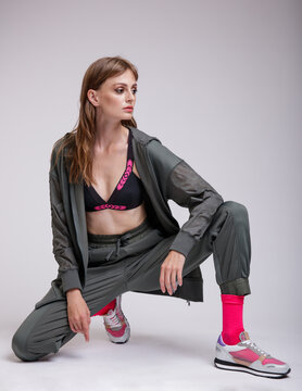 High fashion photo of a beautiful elegant young woman in a pretty green tracksuit, jacket, pants, sports bra, sneakers, pink socks posing over white background. Slim figure. Studio shot.