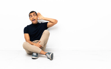 Fototapeta premium African American man sitting on the floor listening to something by putting hand on the ear