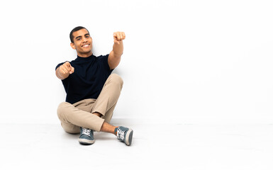 Fototapeta premium African American man sitting on the floor points finger at you while smiling