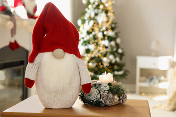 Fototapeta premium Cute Christmas gnome on wooden table in room with festive decorations. Space for text