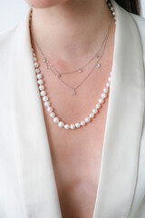 Trending silver necklace with pearls on a beautiful young girl in a white fashionable jacket. Beauty and fashion 
