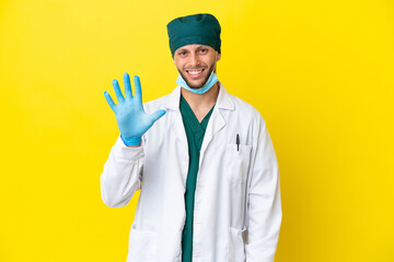 Surgeon blonde man in green uniform isolated on yellow background counting five with fingers