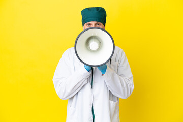 Surgeon blonde man in green uniform isolated on yellow background shouting through a megaphone