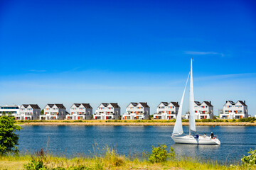 Cottages on a river bank with white sailing ship under a clear blue sky - 0761