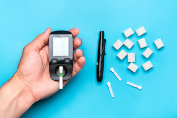 glucometer, sugar cubes on blue background High blood sugar and diabetes concept Top view Flat lay 14 November - World Diabetes Day