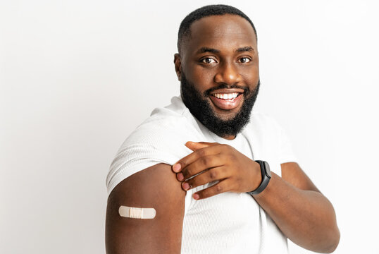 Cheerful Vaccinated African-American Man Showing Arm With Medical Patch And Laughs, Black Male Getting Vaccine Dose Against Covid, Plaster On Her Shoulder, Isolated On White. Healthcare Concept