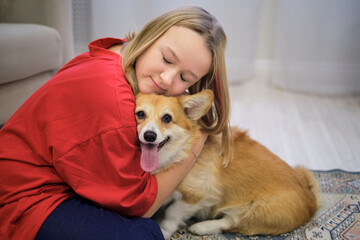 Cute little girl hugging corgi dog with love eyes closed, smiling. Dog lover with domestic animal