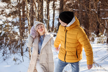 Loving couple in warm clothes is spending Christmas vacation outdoors in the snowy countryside.