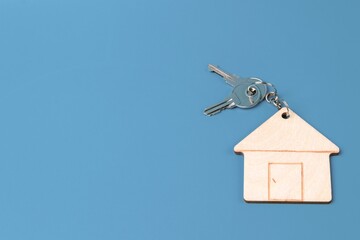 Wooden house keychain with keys on a metal chain on a blue background. Home buying concept