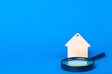 Keychain Wooden house and magnifier on a blue background. Housing search concept