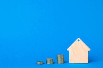 Keychain Wooden house and stacks of coins on a blue background. Home buying concept