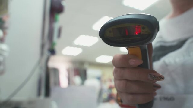 Barcode scanner flashes red beam close-up. Female salesperson scans a quick response in the store. Scanner reads Quick Response reply in shop