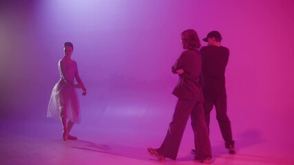 Couple dancing hip hop and woman showing ballet on pink neon background. Young dancers having battle. Modern dance school for teenagers. Different performing art styles. 