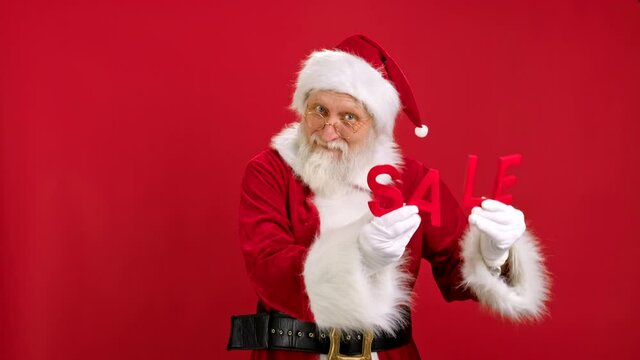 Cheerful Santa Claus is Happy With Big Discounts at Christmas Black Friday Dancing Holding Red Letters With Word SALE on Red Studio Background. Discount sale, Black Friday, Cyber Monday.