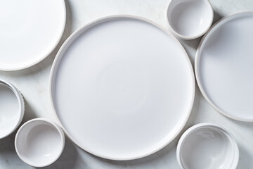 Empty white plates and bowls on white kitchen table.  Overhead view.