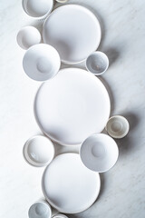 Empty white plates and bowls on white kitchen table.  Overhead view.