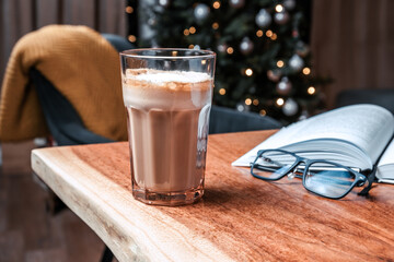 Coffee and book on wooden table with Christmas tree background