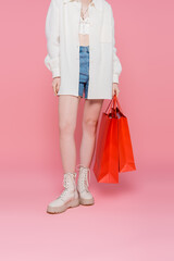 Cropped view of young stylish woman holding shopping bags on pink background